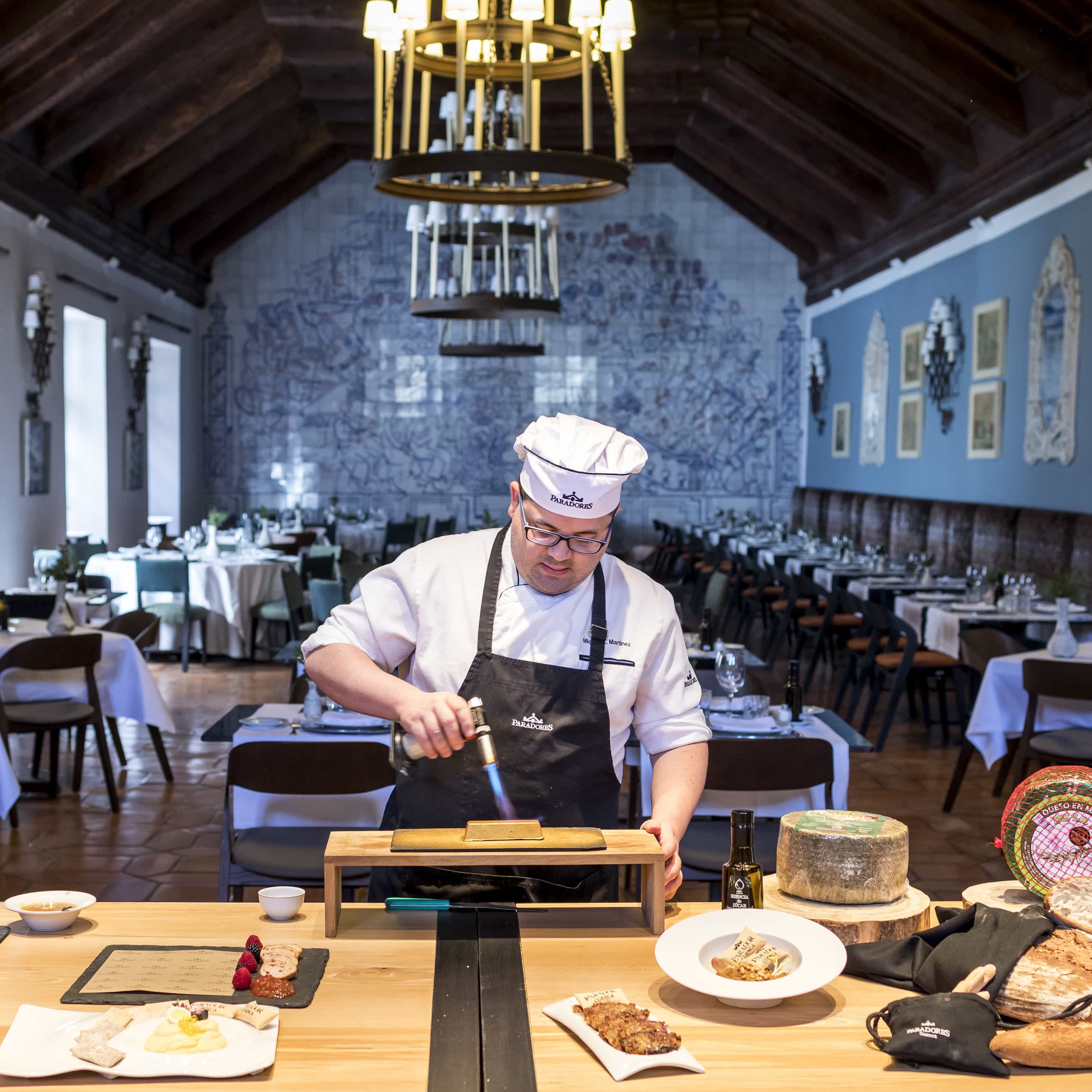 Chef del Restaurante del Parador de Cuenca caramelizando postre con soplete flambeador en el comedor interior