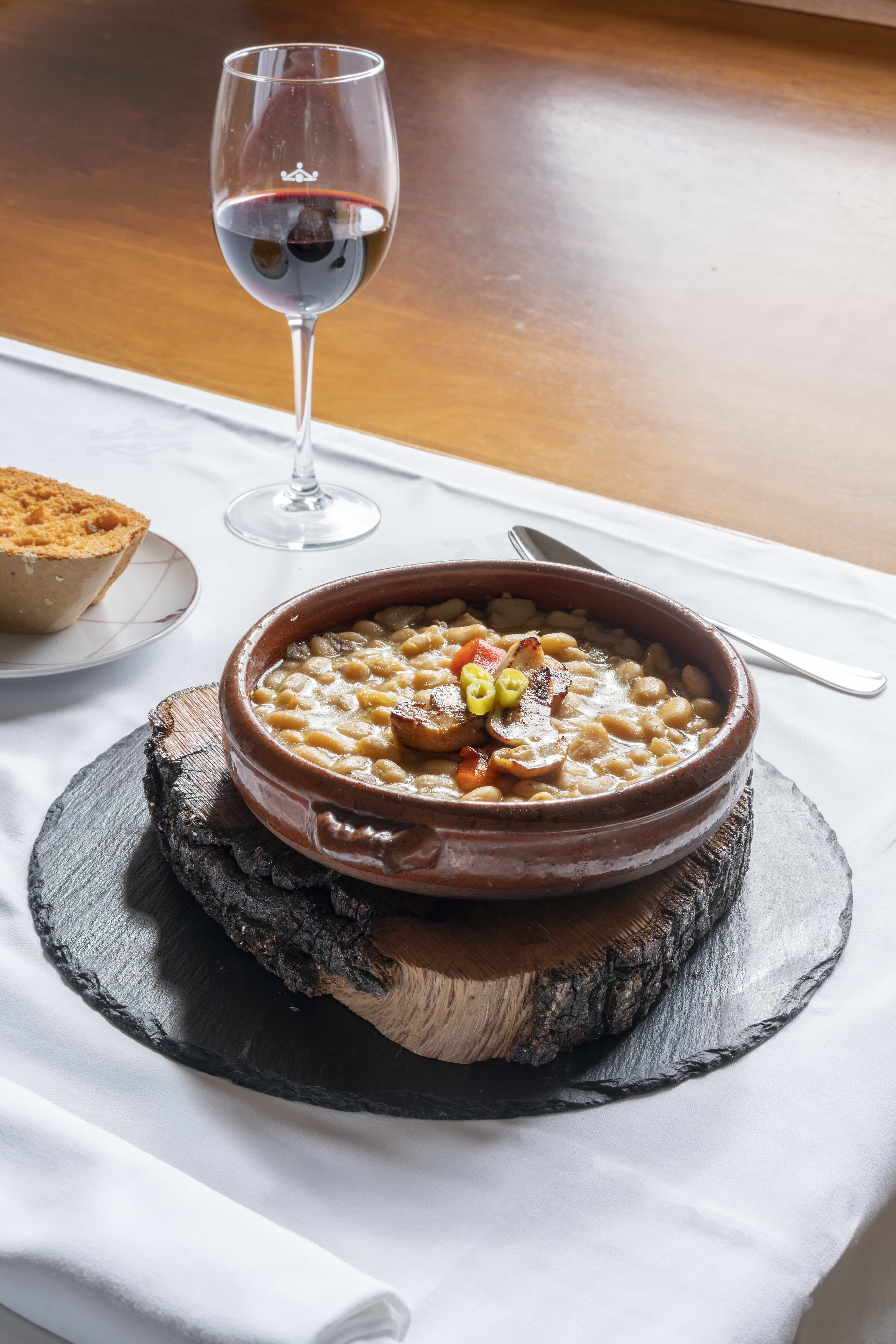 Plato de cuchara en cazuela de barro con copa de vino del Restaurante del Parador de Gredos