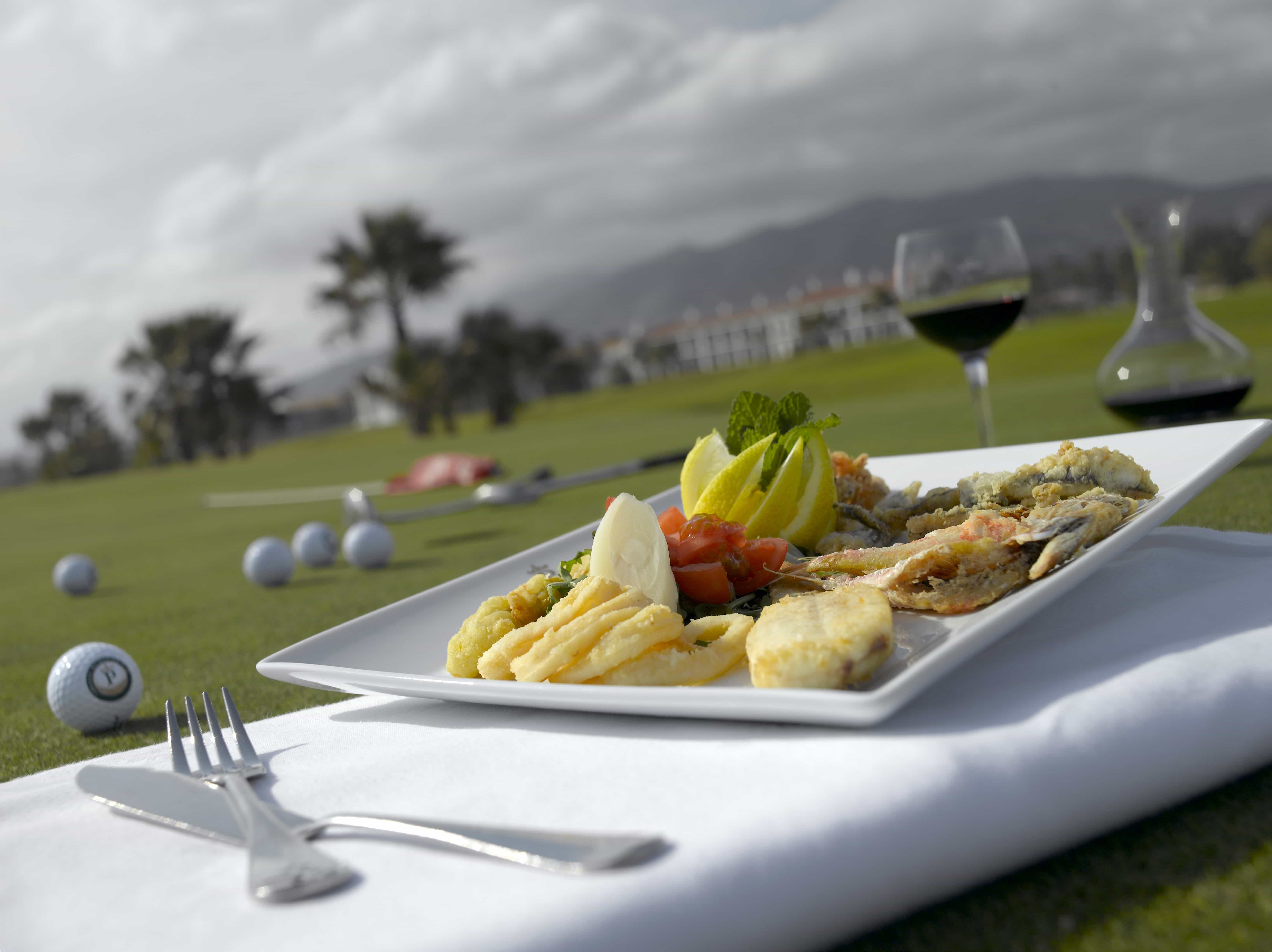 Detalle de plato con base marinera con el campo de golf al fondo del Restaurante El Green del Mediterráneo