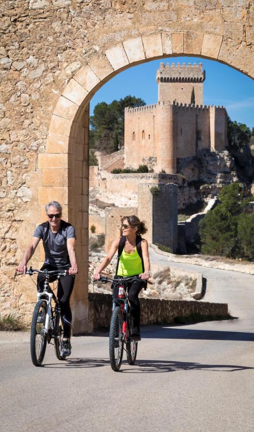 Una pareja monta en bicicleta con el Parador de fondo