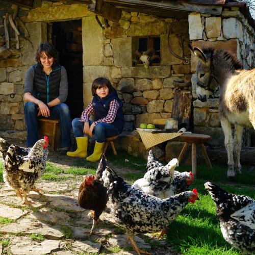 Imagen de la actividad La Ruta de Pepín dentro del programa Naturaleza para los Sentidos en el Parador de Cangas. Una mujer y un niño frente a una cabaña de pastor rodeados de gallinas y un burro.